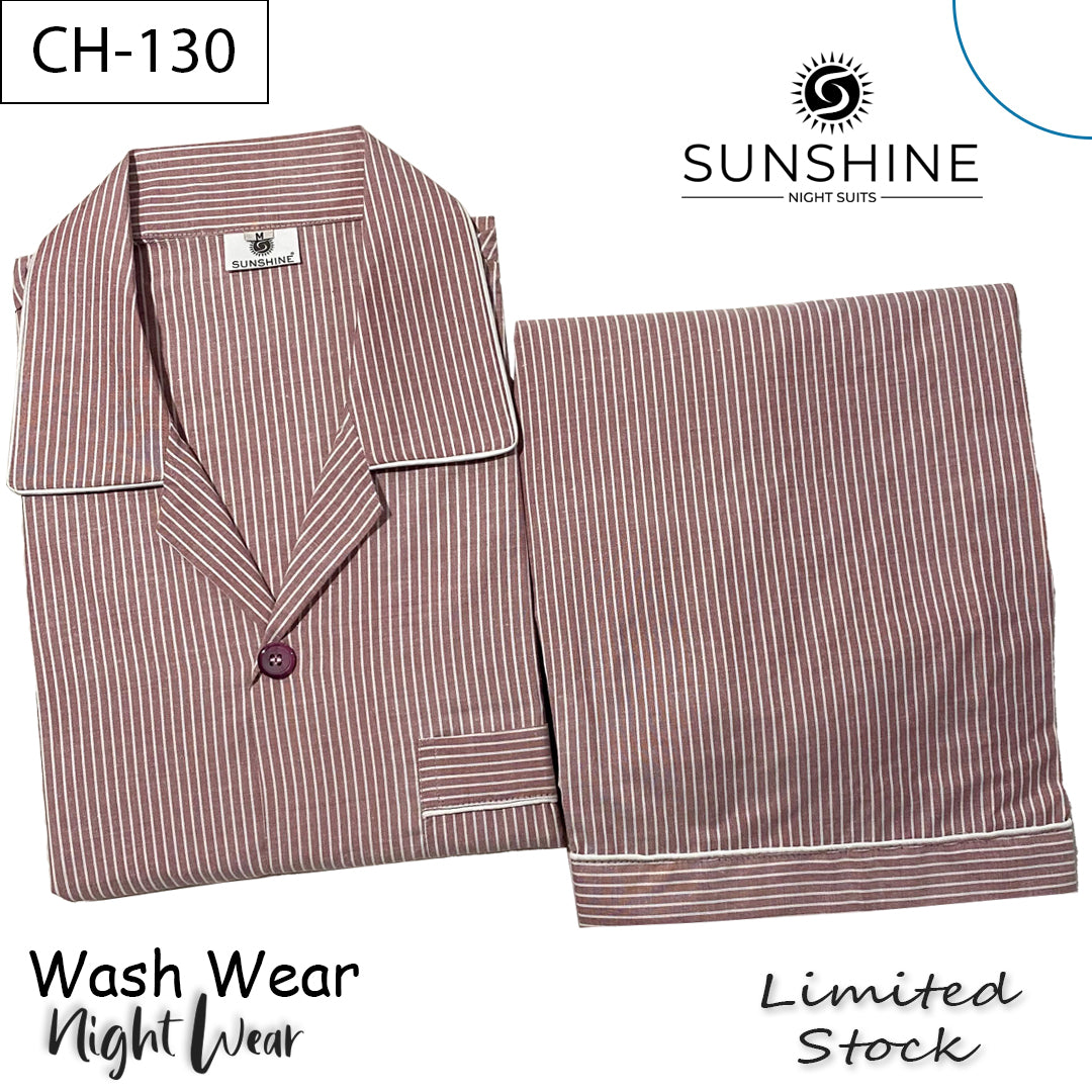 A male model smiling and standing in a cozy bedroom wearing a maroon and white striped wash-and-wear pajama set (CH-130). The long-sleeve shirt has a front pocket with perfectly aligned stripes, button closure, and white piping on the collar and cuffs.